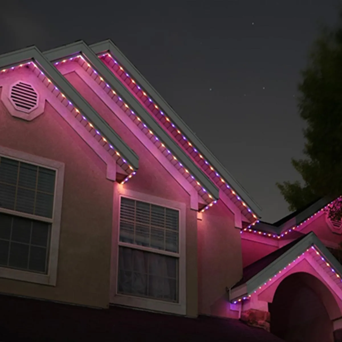 Gabled stucco home at night washed in pink permanent roofline lighting